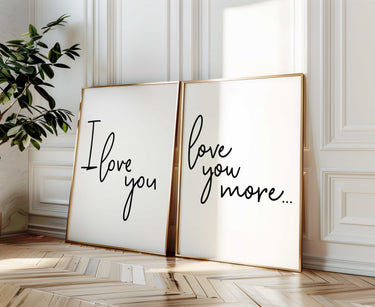 Minimalist set of two typography wall art prints reading “I Love You” and “Love You More” in black script lettering displayed in gold frames against a bright neutral interior wall.