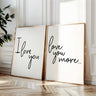 Minimalist set of two typography wall art prints reading “I Love You” and “Love You More” in black script lettering displayed in gold frames against a bright neutral interior wall.
